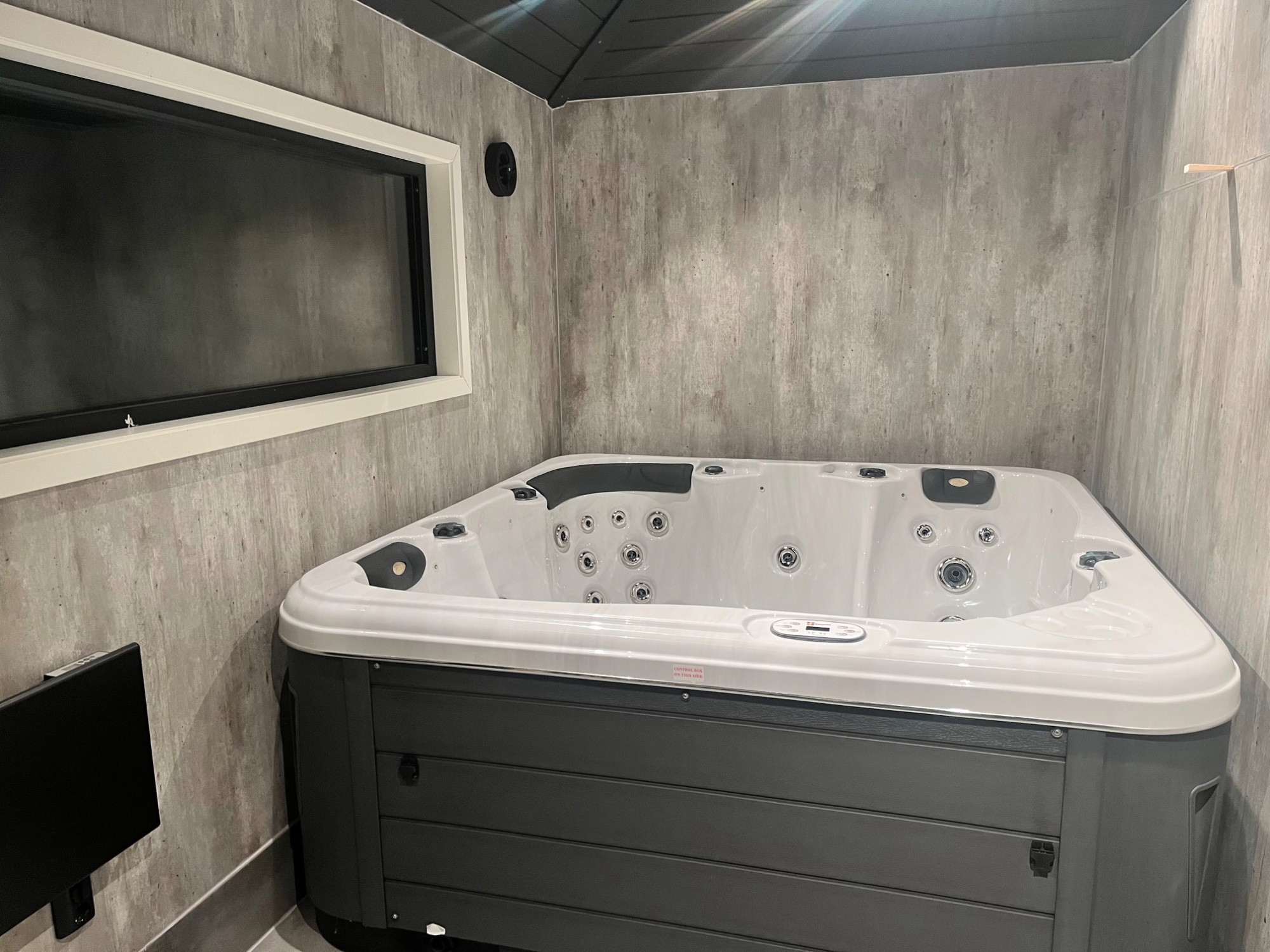 Innvendig rom med boblebad, betongpanel på vegg og mørkt tak